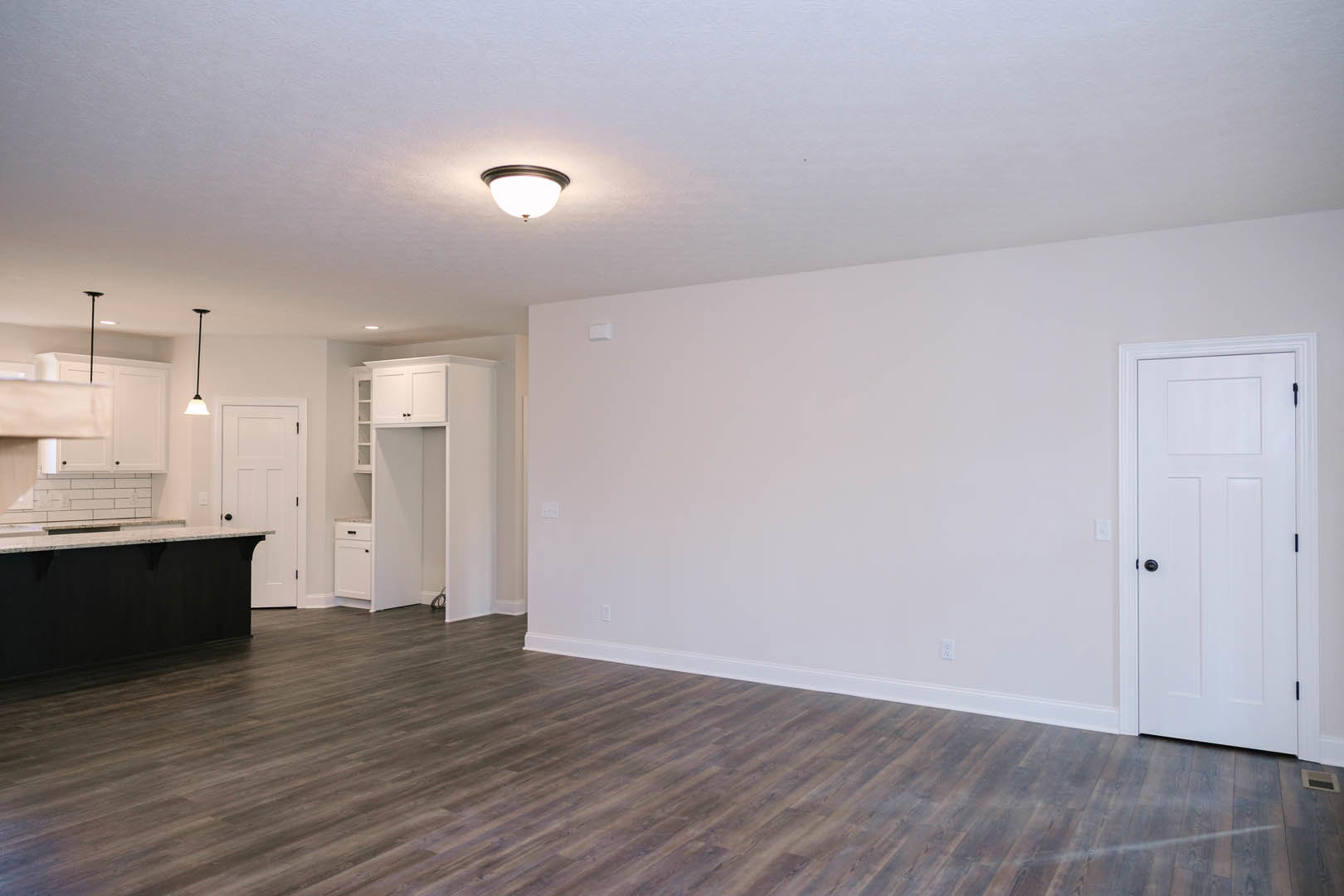 Kitchen with wood flooring, white walls, white cabinetry with black knobs, marble countertops, and a ceiling light fixture