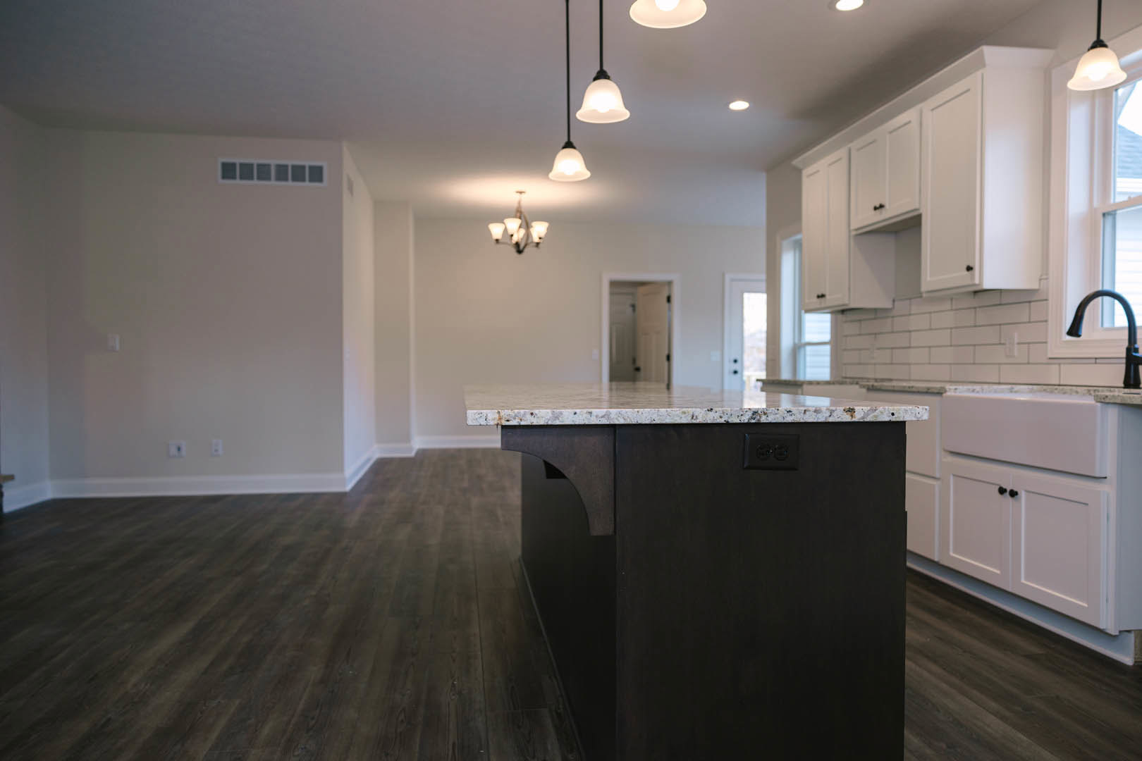 Kitchen with white shaker cabinets, marble island countertop, black hardware, stainless faucet, tile backsplash, square window, and wood flooring