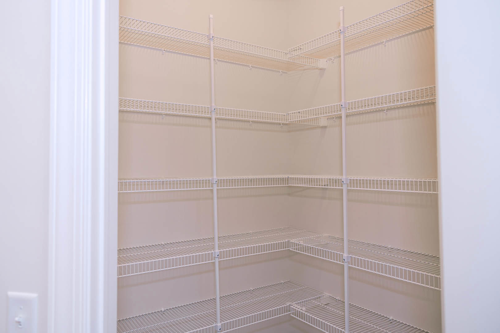 White wire shelving installed against a smooth white wall in a closet, with a light switch visible nearby.