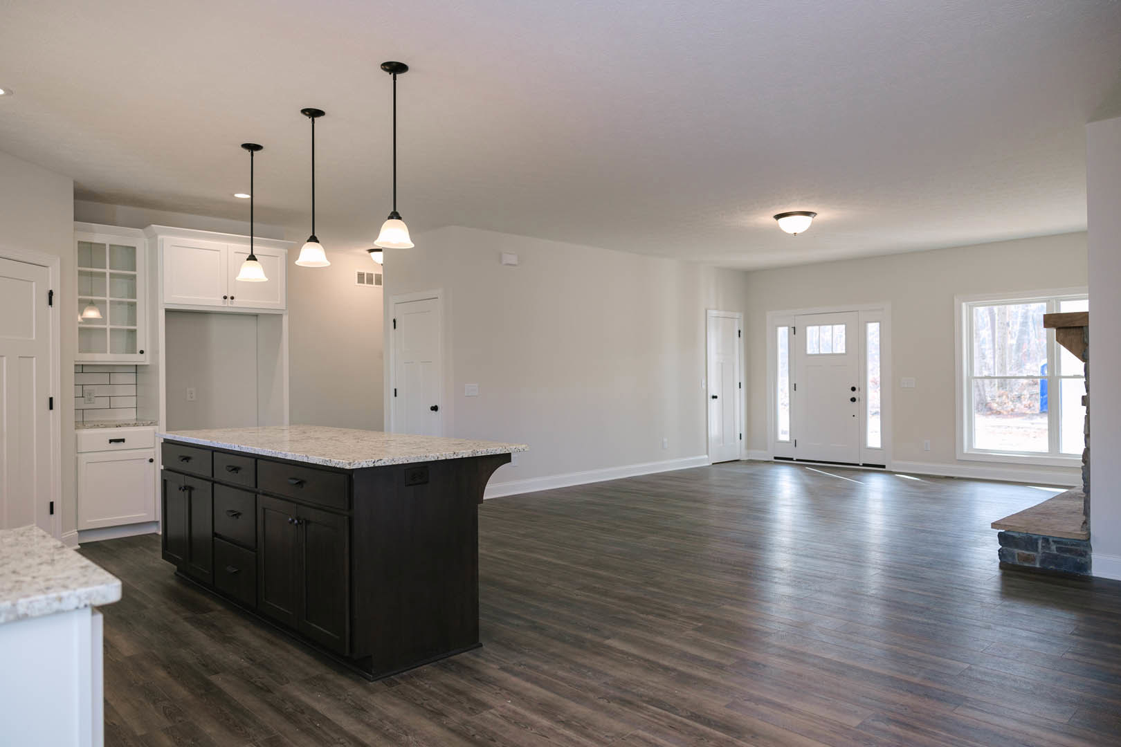 Spacious kitchen featuring a large marble-topped island, wood flooring, white cabinetry, glass-paneled door, and windows overlooking the outdoors