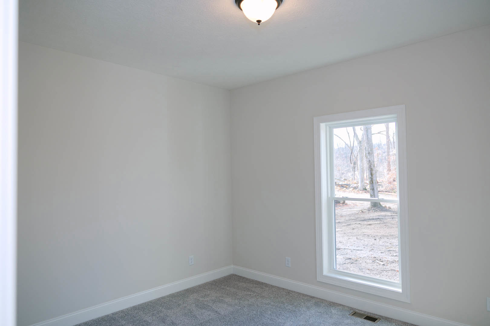 Carpeted bedroom with large window overlooking forest, white plaster walls, ceiling vent, and recessed lighting