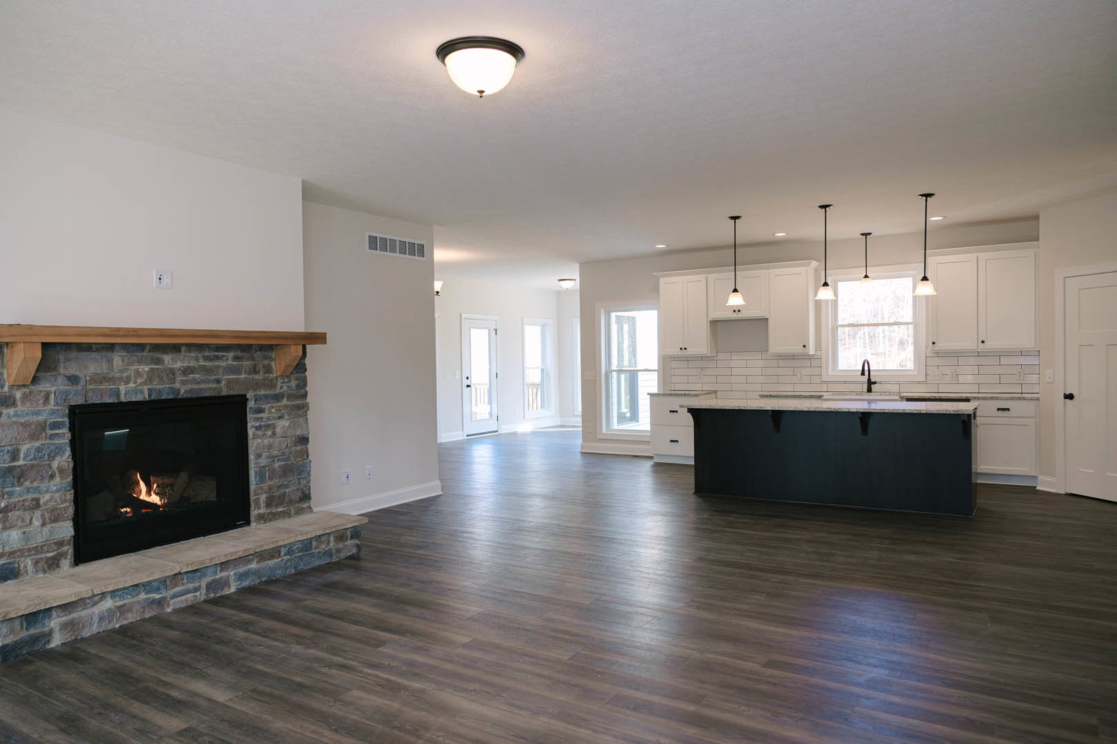 Living room featuring stone fireplace with active fire, hardwood flooring, light fixture on white ceiling, and partial view of countertop