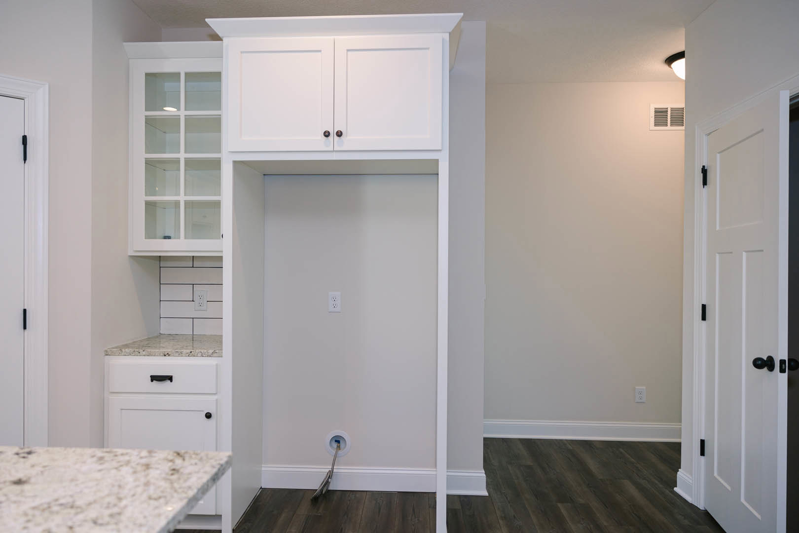 White kitchen featuring marbled countertops, glass-front cabinets with black handles, and a hose emerging from a wall opening.
