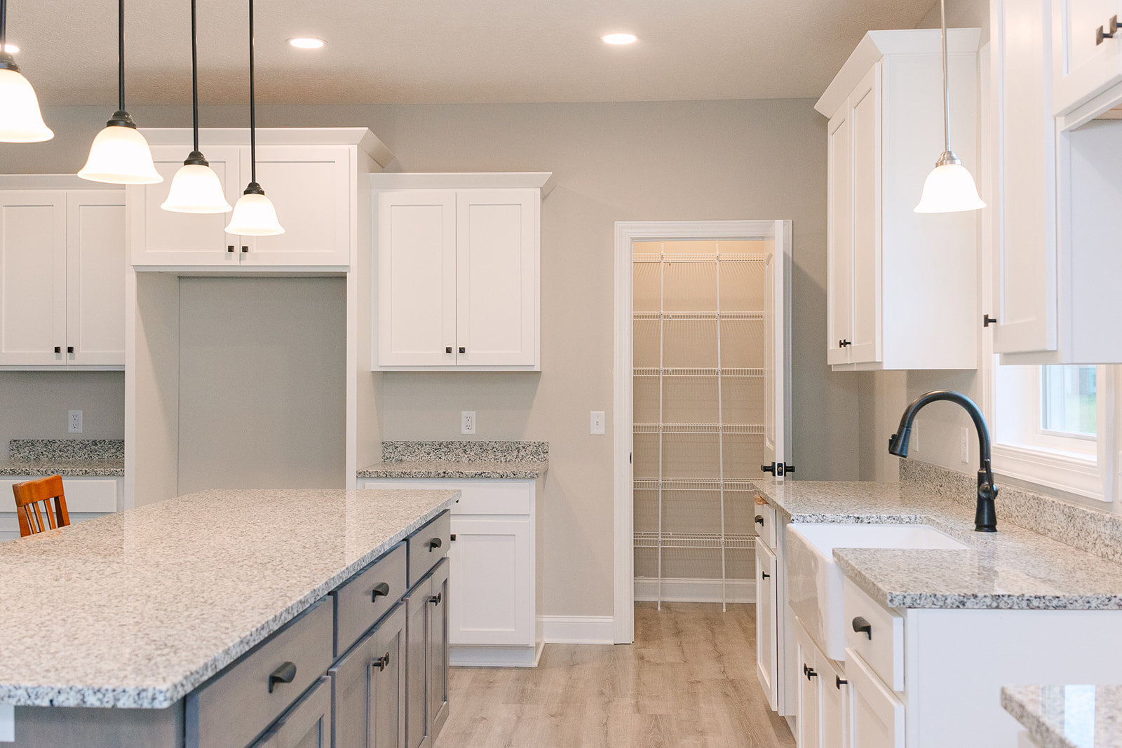 Granite countertops, white cabinets with black handles, black faucet, tile backsplash, drawers, and a chair in a modern kitchen