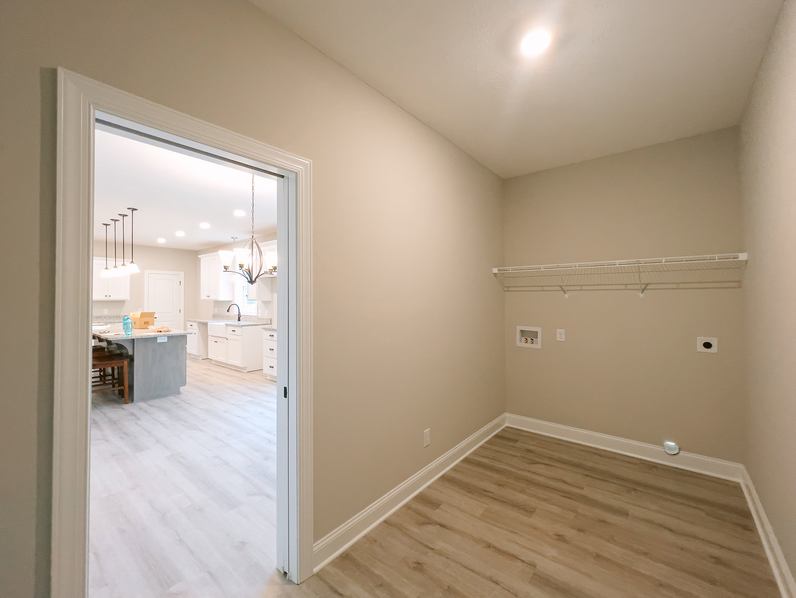 Open kitchen with white cabinetry, central island and sink, wood flooring, dining table with chairs, white trim along walls, recessed ceiling lighting