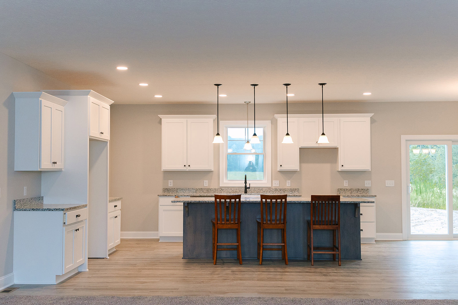 Modern kitchen featuring a bar-height counter with wooden chairs, cushioned seats, glassware on the counter, white cabinetry, glass-paneled door, and light flooring.