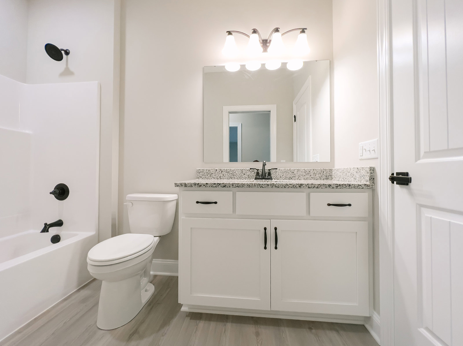 Bathroom with white toilet and pedestal sink, three-light fixture above mirror, white door with matching frame, light gray tile floor, neutral walls.
