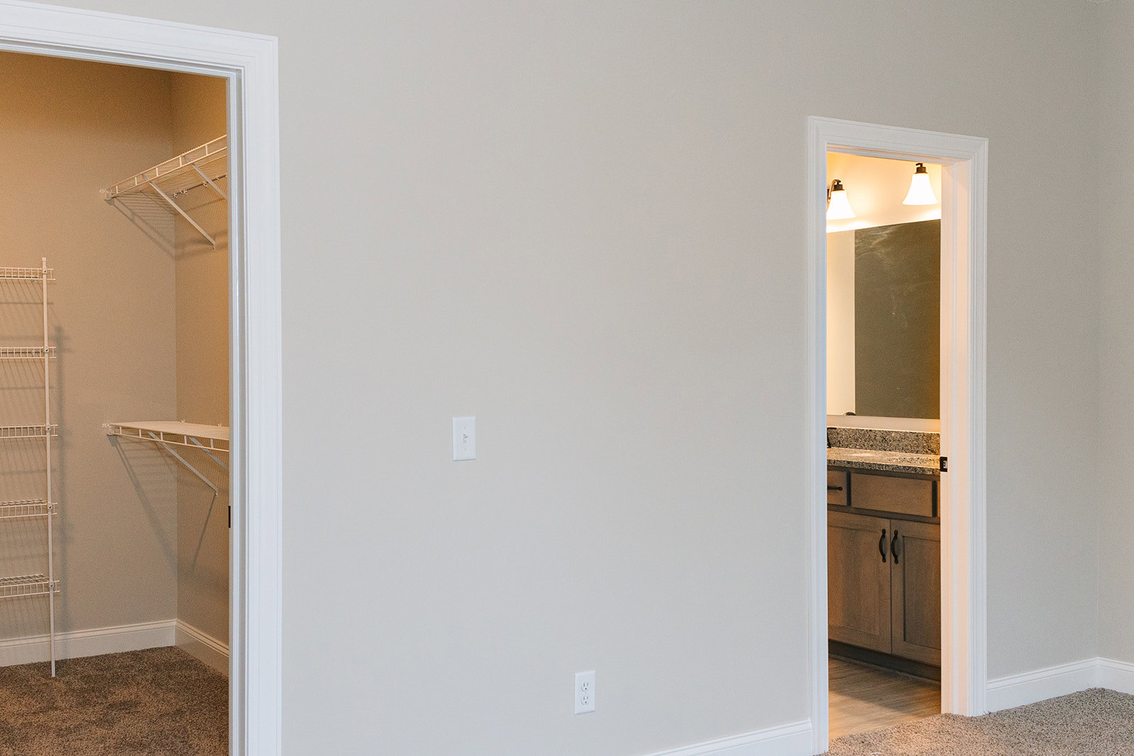 Walk-in closet with white shelving, open door leading to bathroom, white metal railing on wall, mirror reflecting room, close-up lamp on shelf, plaster walls and cabinetry