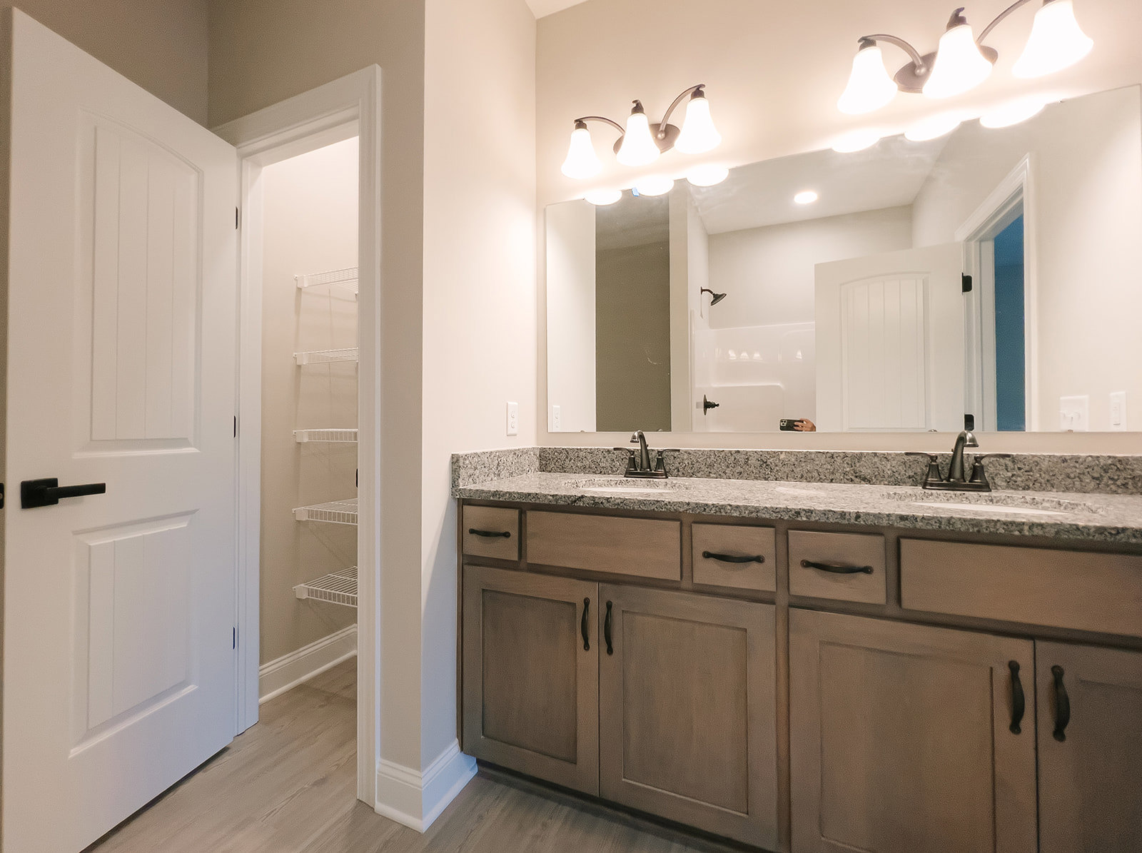 Bathroom with double vanity featuring white countertop, undermount sinks, black faucets, large frameless mirror, light fixture above, white cabinetry with black handles, white door