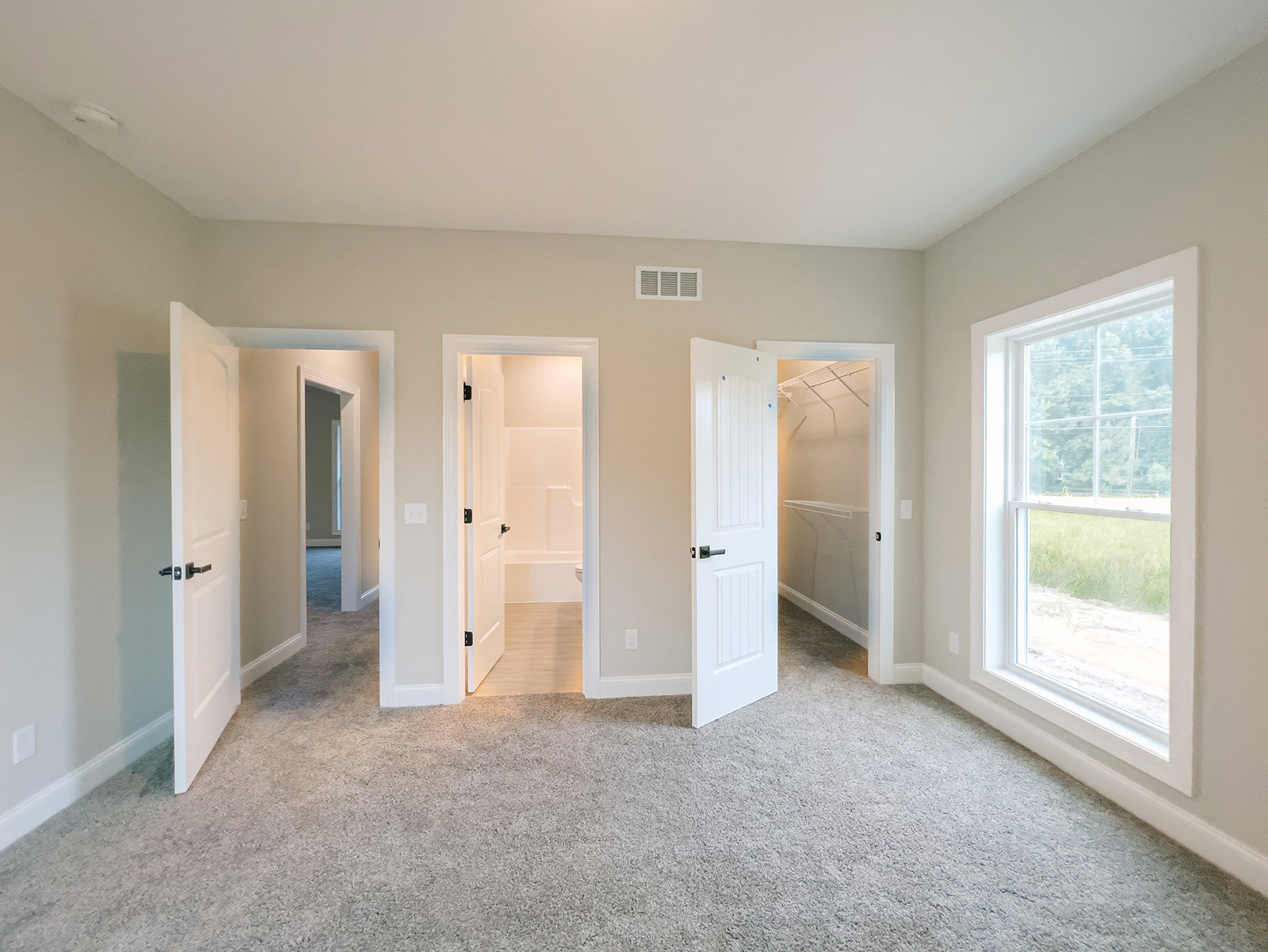 White-walled room with multiple white doors, carpeted floor, open bathroom door, window showing outdoor view, and white closet shelf