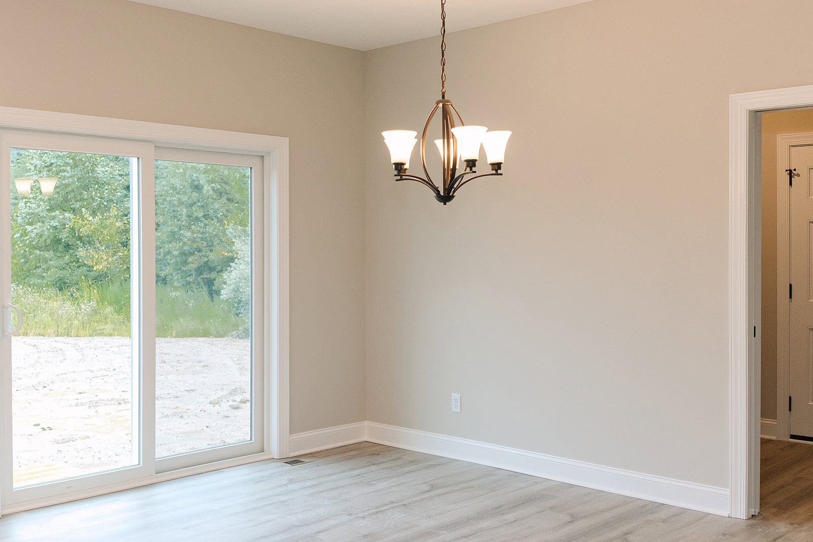 Modern chandelier hanging in a bright room with white wood flooring, white trim, and a glass door leading outside.
