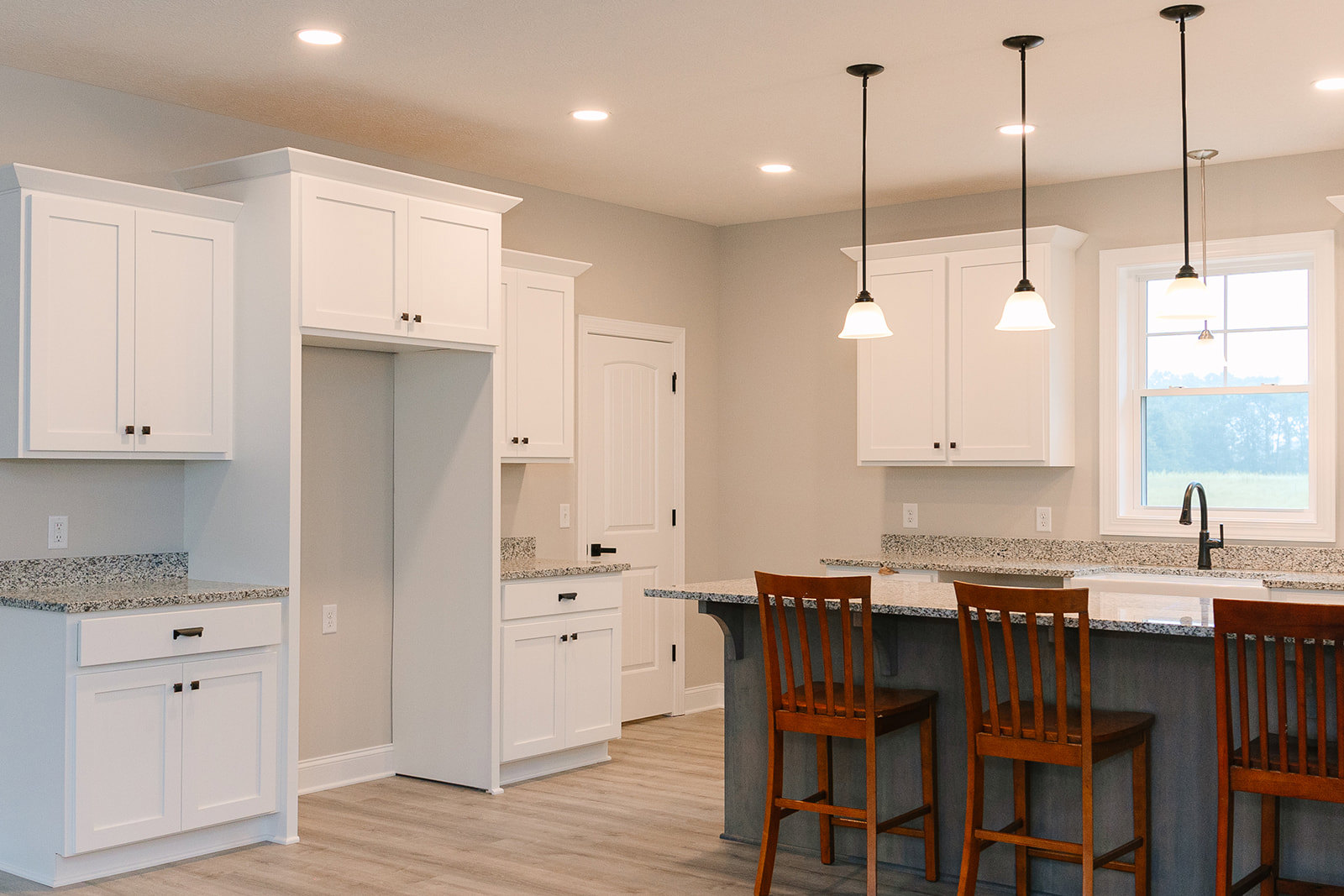 Open kitchen with white cabinetry, marble countertop bar, wooden stools, stainless steel appliances, and light wood flooring