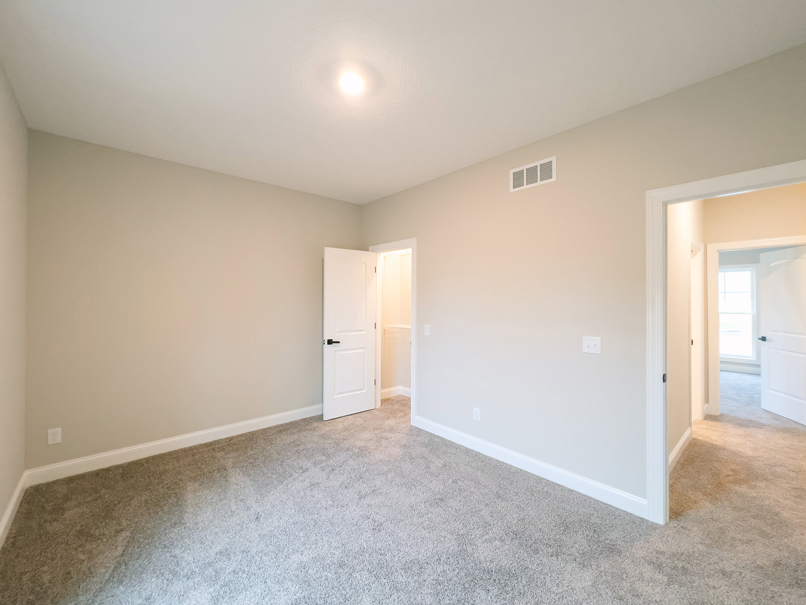 Carpeted room with white door featuring black handle, white walls, ceiling vent, and crown molding
