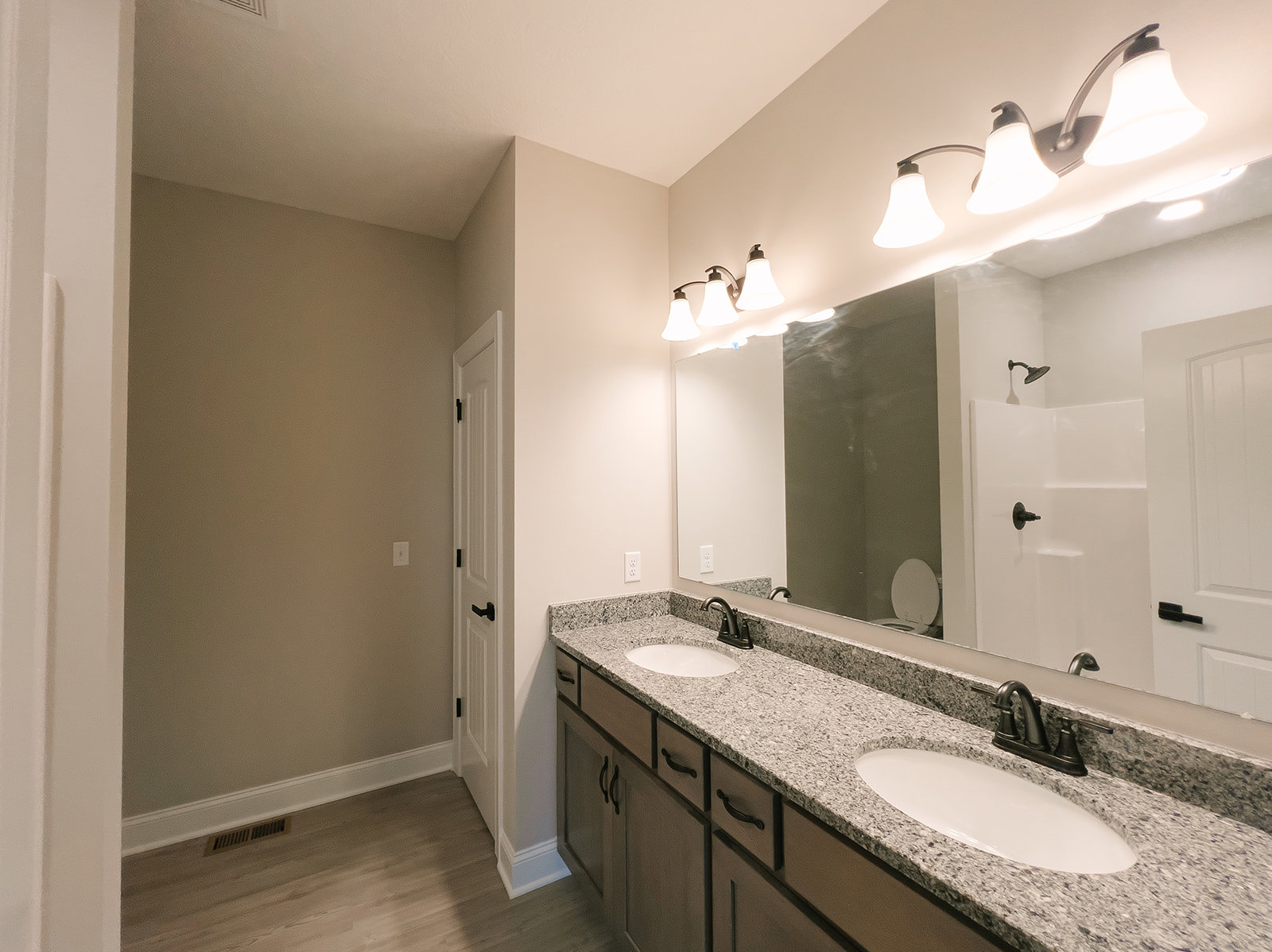 Bathroom with double white sinks, large framed mirror, black metal faucets, white cabinetry, three-light fixture with white shades, wall vent, and tiled backsplash.