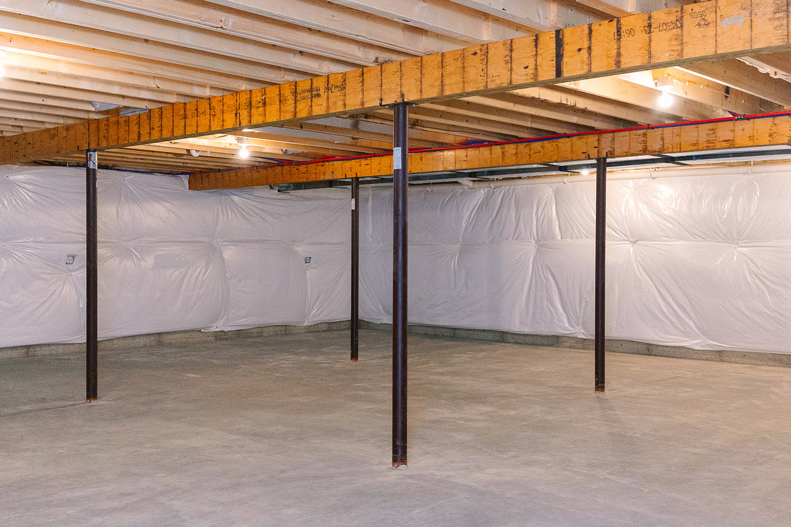 Basement room with exposed wooden ceiling beam, black metal support pole featuring a blue stripe, white painted wall, and concrete floor
