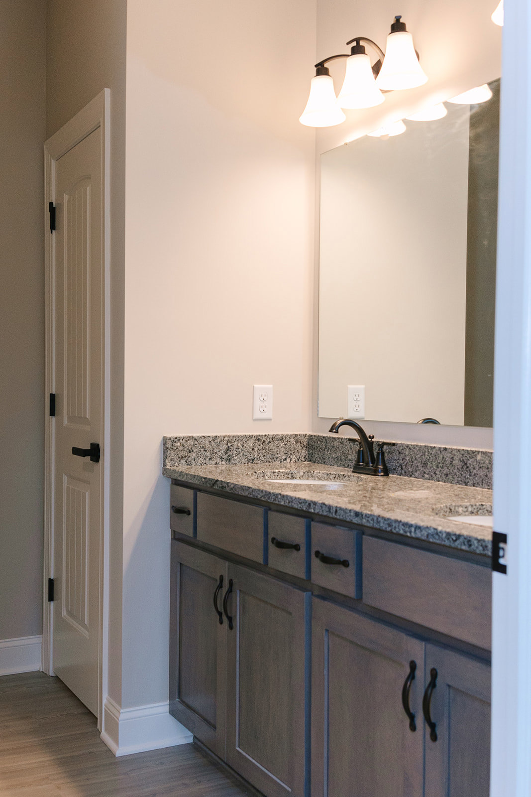 Bathroom with granite countertop sink, chrome faucet, wall-mounted mirror, white cabinetry, tile backsplash, and visible electrical outlet