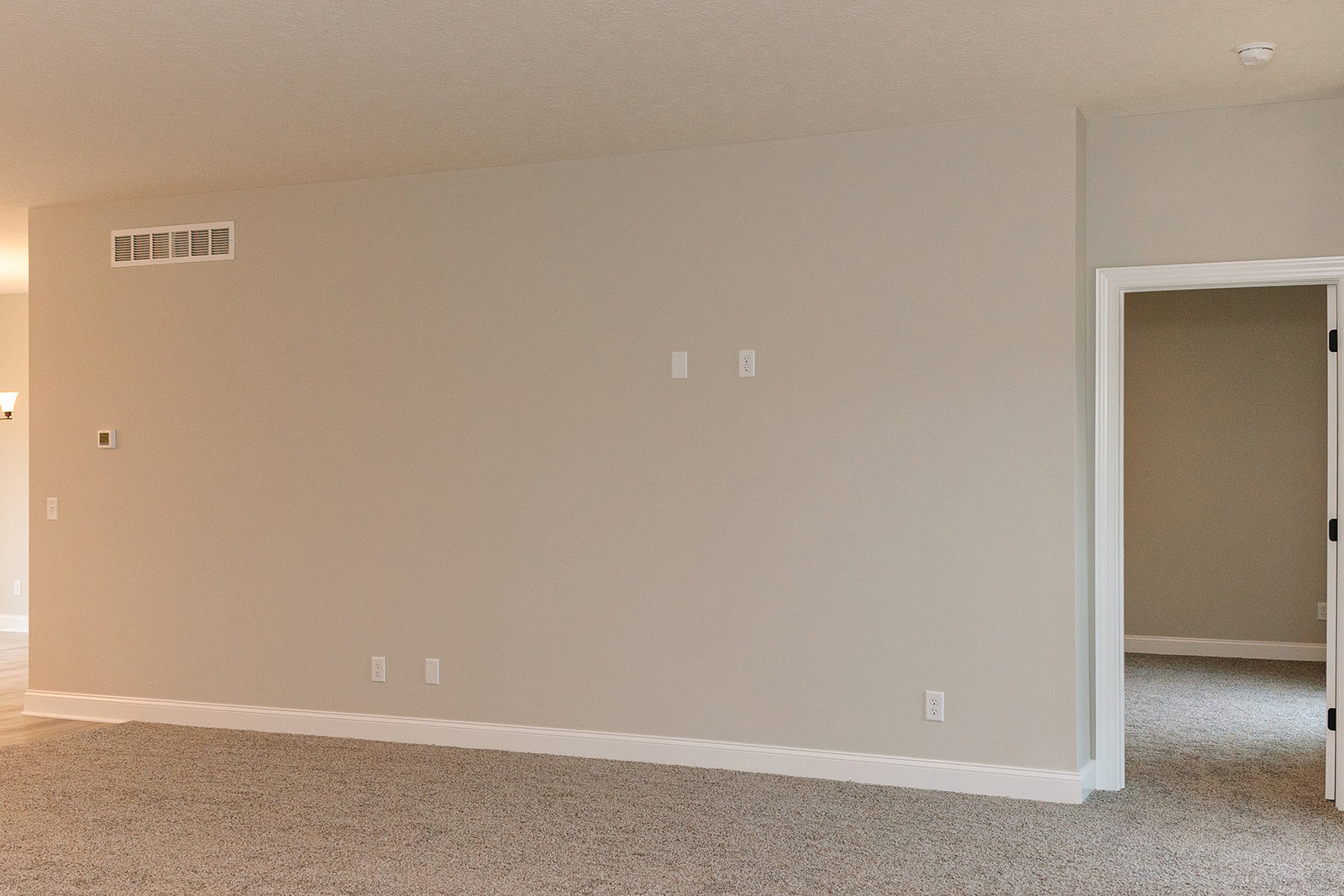 White carpeted floor, open white door, white plaster walls, ceiling vent, and smooth white ceiling in a residential interior room