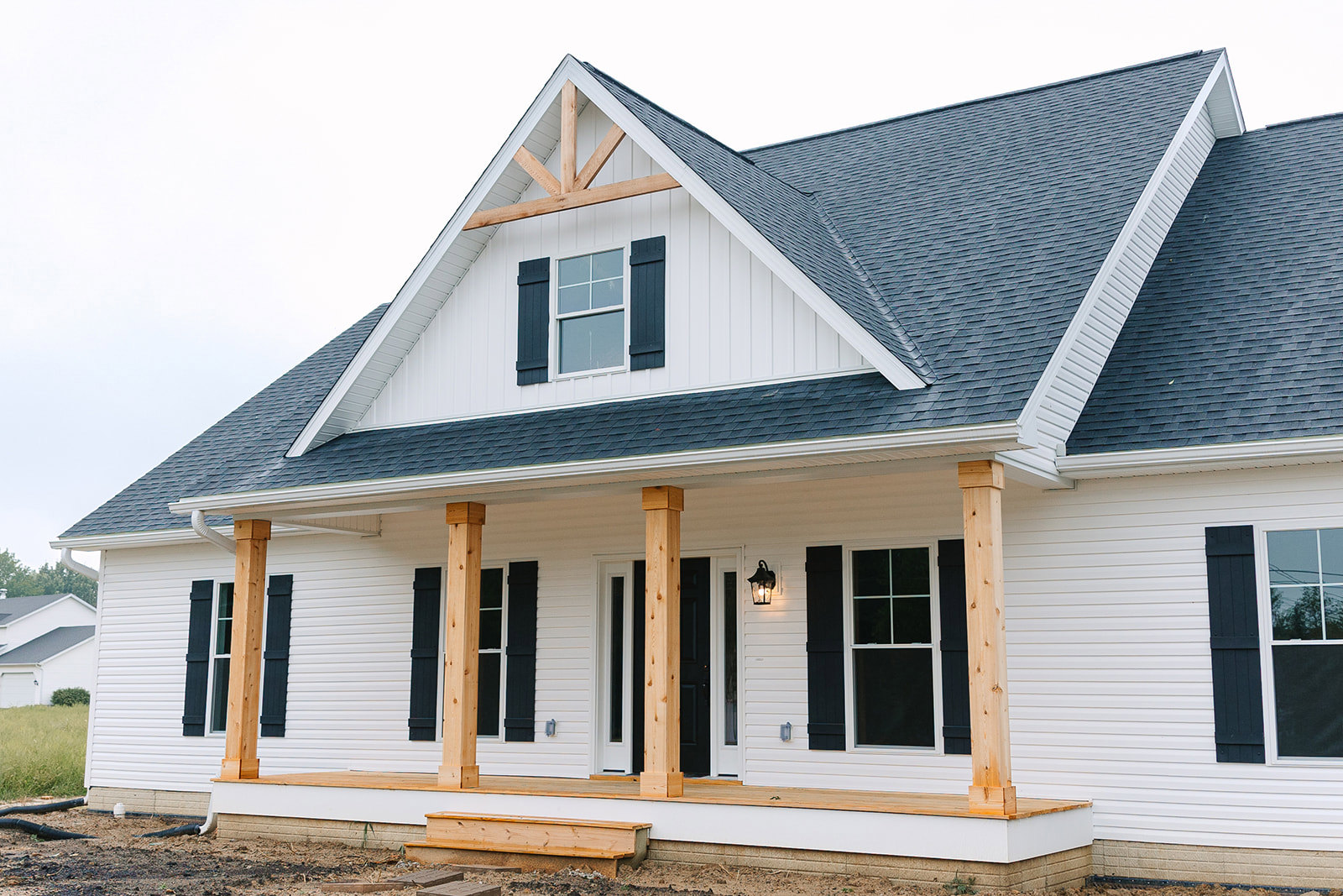 White siding house with grey roof, black shutters, white-framed windows, and covered front porch