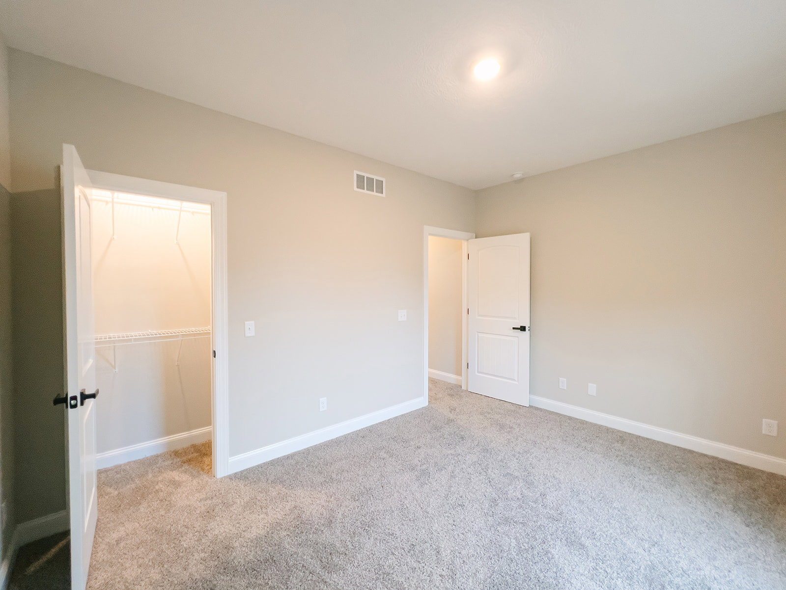 Carpeted bedroom with white walls, open closet door, black door handle, ceiling vent, and overhead light fixture