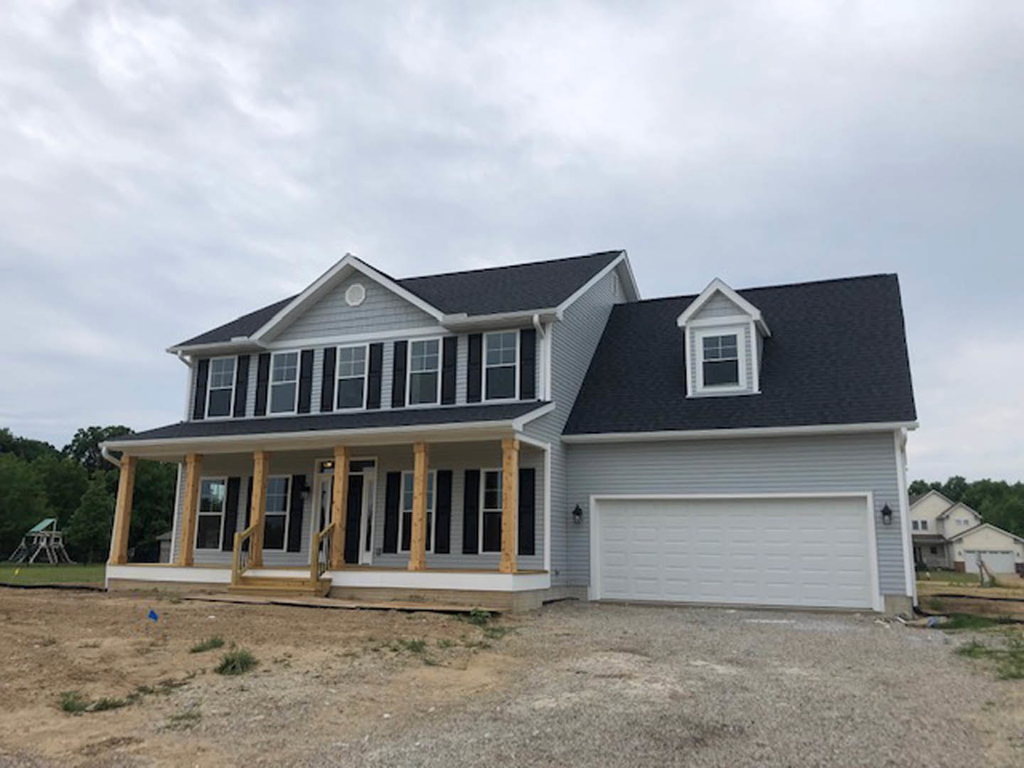 Two-story house under construction with white siding, white-framed windows, attached garage featuring a white door, and a paved driveway; cloudy sky overhead.
