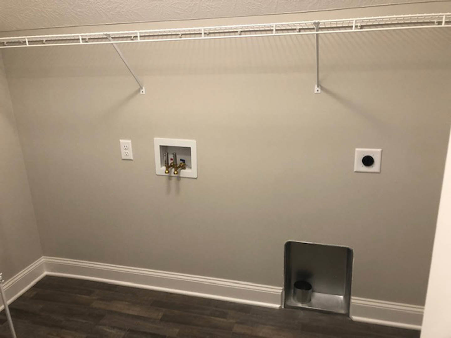 White plaster bathroom wall with white curtain rod, wall-mounted electrical outlet and switch, black circular button on white plate, and white pipe against white surface.