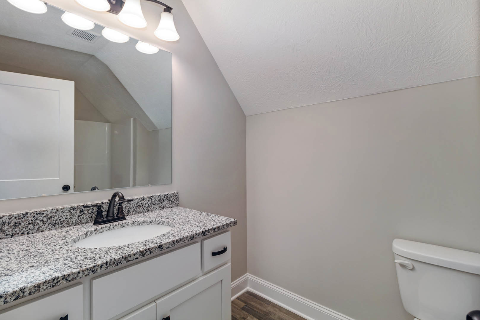 Bathroom with marble countertop, undermount sink, chrome faucet, white toilet, tile flooring, and shaker-style cabinetry