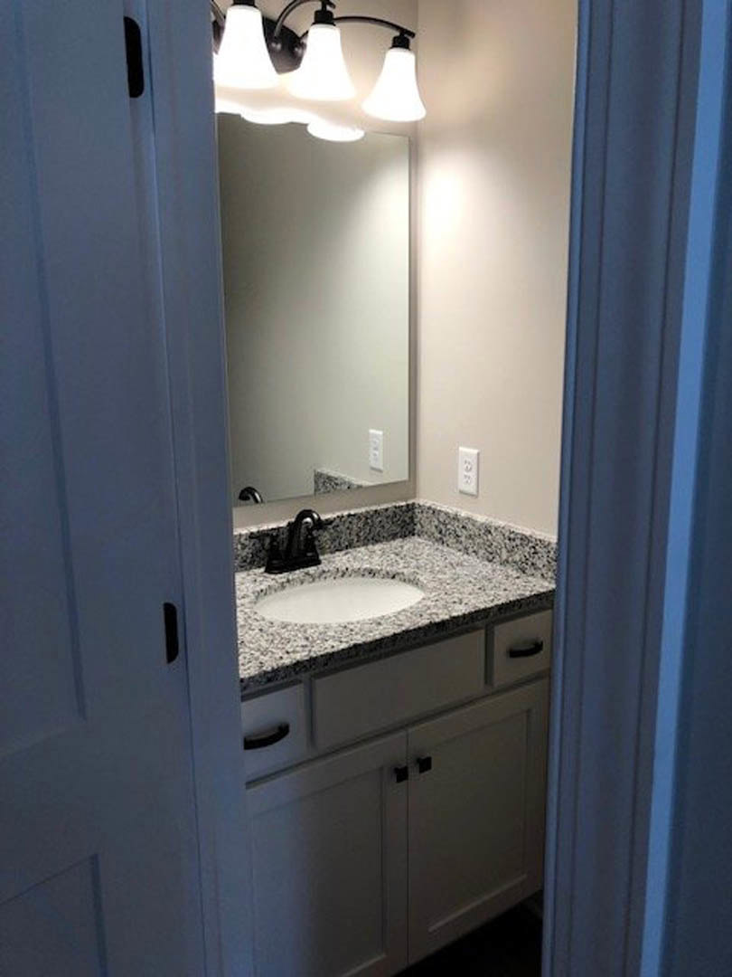 White quartz countertop with undermount sink, chrome faucet, dark wood cabinetry, large framed mirror, and three-bulb wall sconce above.