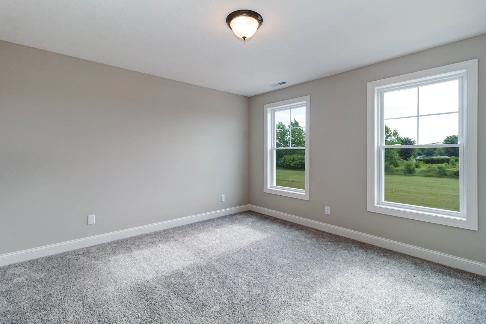 Carpeted room with multiple windows overlooking grassy field and trees, white walls, ceiling light fixture, simple molding