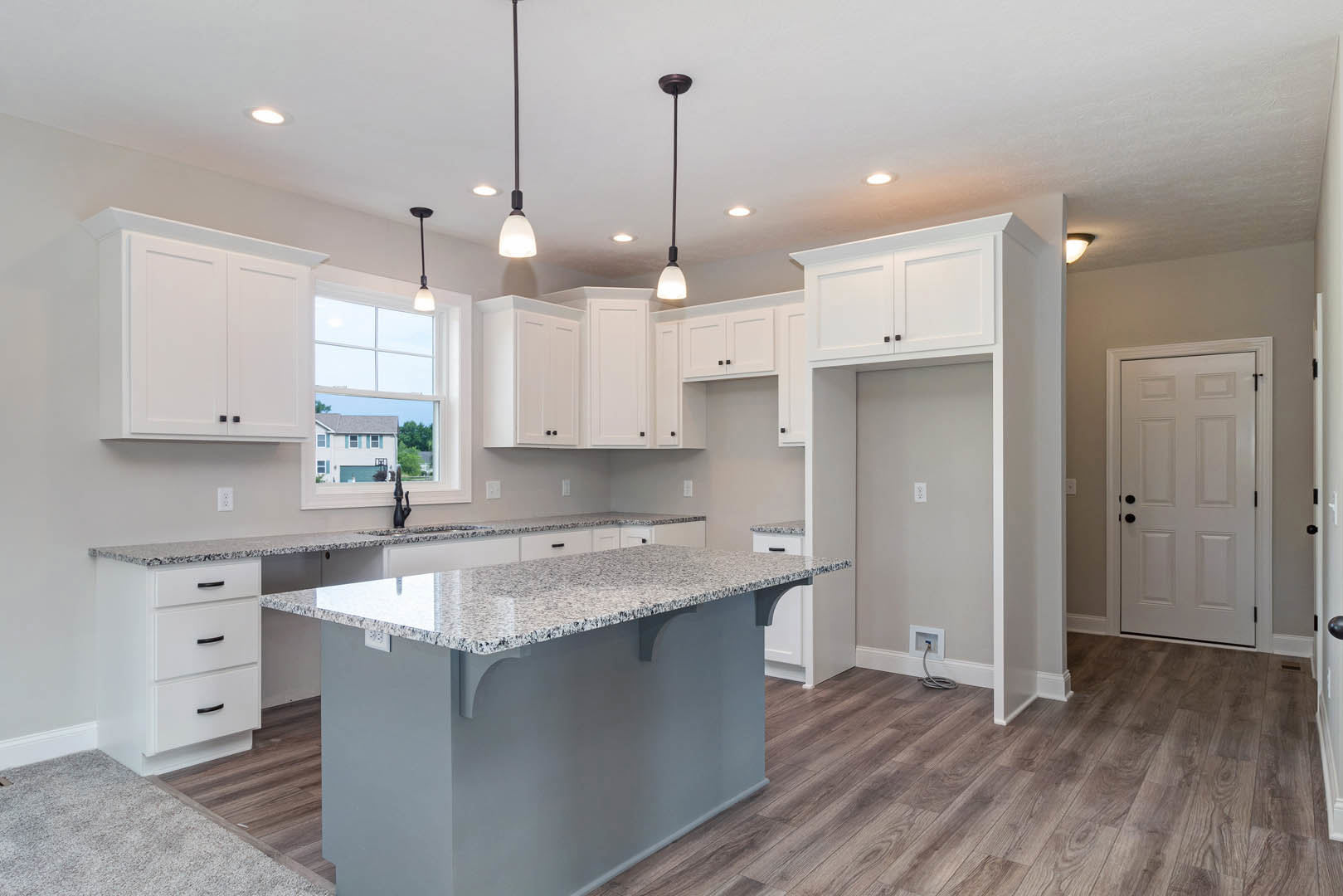 Marble island with waterfall edge, white cabinetry, stainless steel sink, tile backsplash, light wood flooring, recessed lighting, and black hardware on doors and drawers