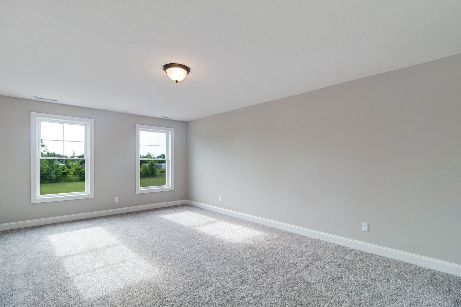 Carpeted room with two large windows overlooking a green lawn, white plaster walls, and a modern ceiling light fixture