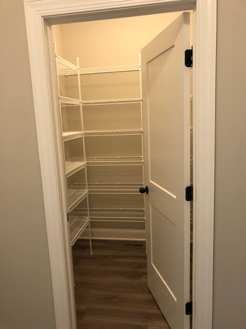 Walk-in closet with white shelves, open white door, wood flooring, and white walls