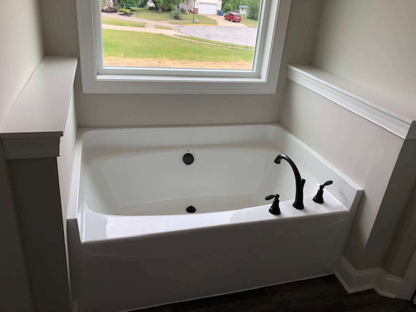 Freestanding white bathtub with matte black faucet beneath a large window in a bright bathroom