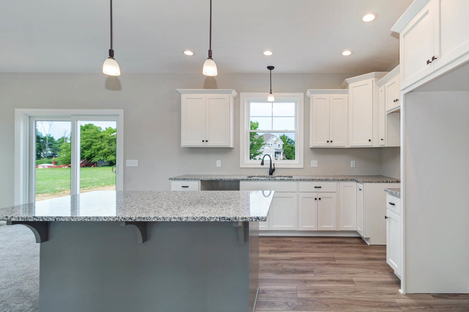 Granite countertops, white shaker cabinets, stainless steel sink, modern light fixture, window overlooking green lawn