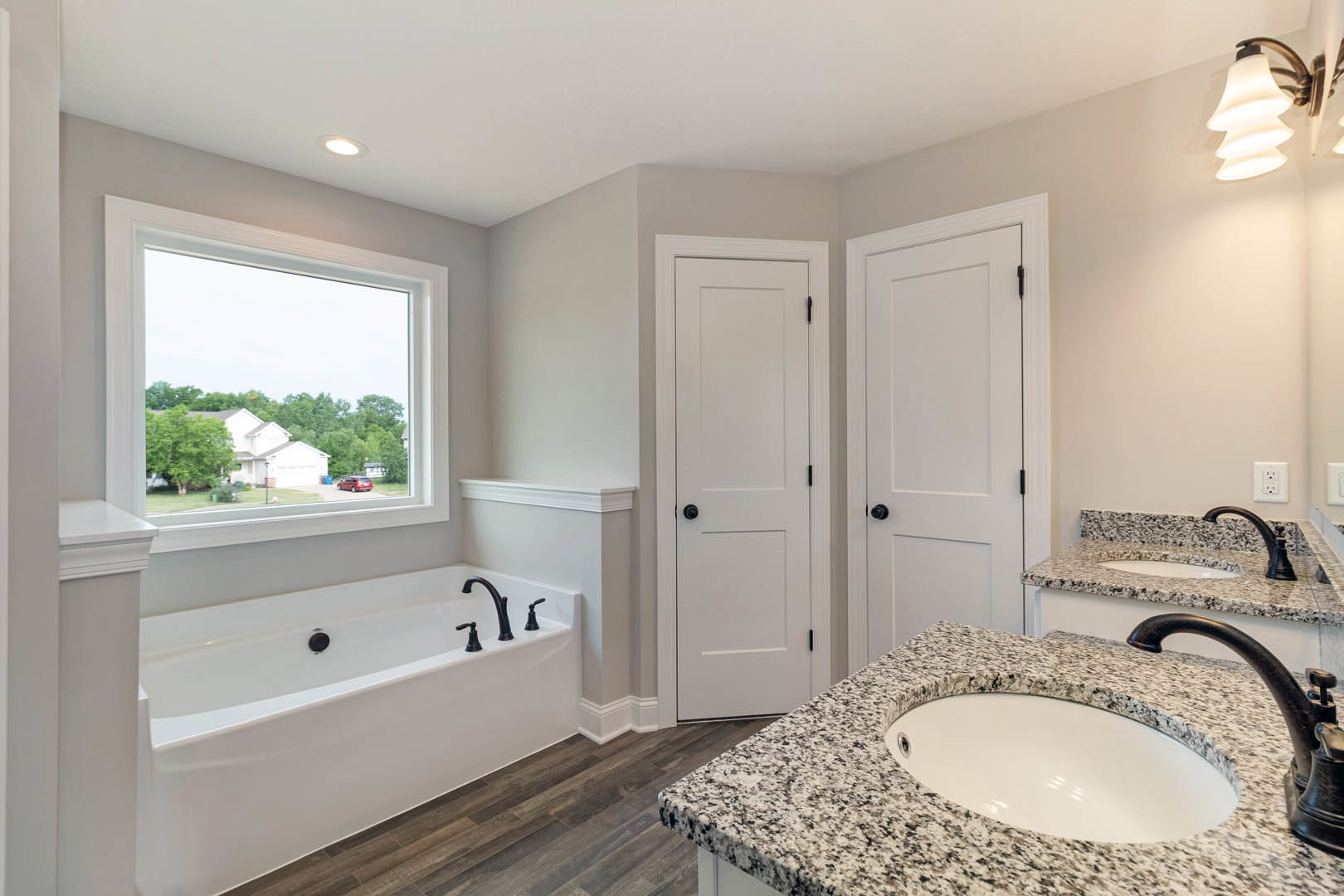 Bathroom featuring marble countertop with undermount sink, freestanding bathtub with chrome faucet, white door with black hardware, window overlooking trees and houses, and modern