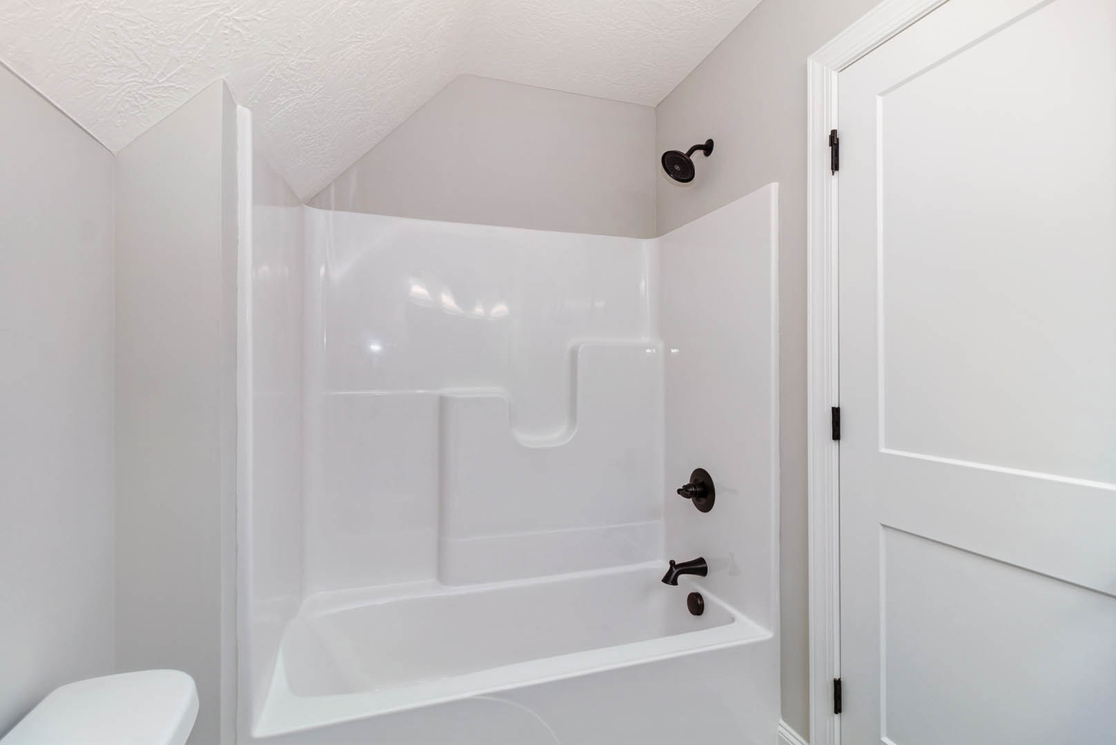 Freestanding white bathtub with matte black faucet and fixtures, surrounded by light tile walls, wall-mounted shower head, and partial view of white door