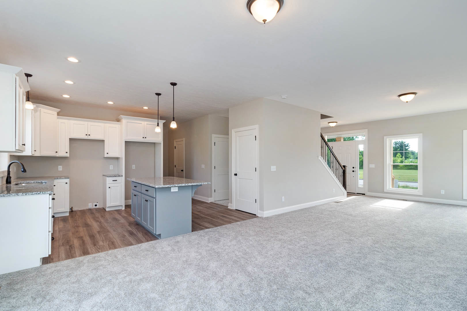 Open-concept living room and kitchen featuring a marble-topped island, white cabinetry, stainless sink, white refrigerator with black handle, white door with black knobs, wood