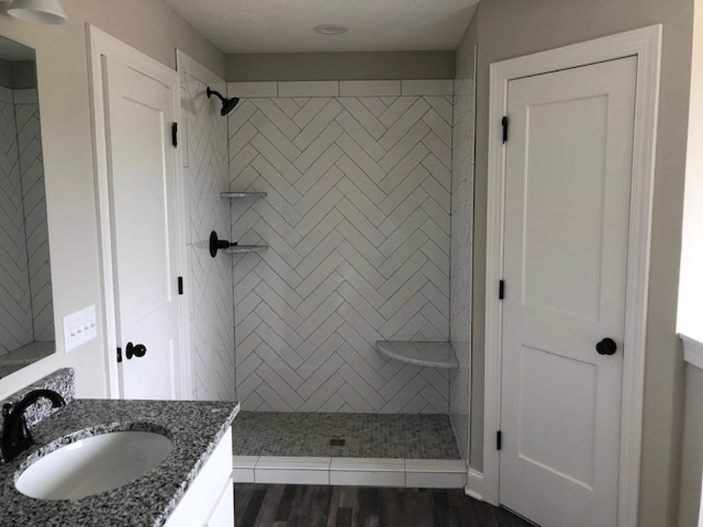 Modern bathroom featuring a white sink with black speckled countertop, glass-enclosed shower, light gray tile walls, chrome fixtures, and minimal decor.