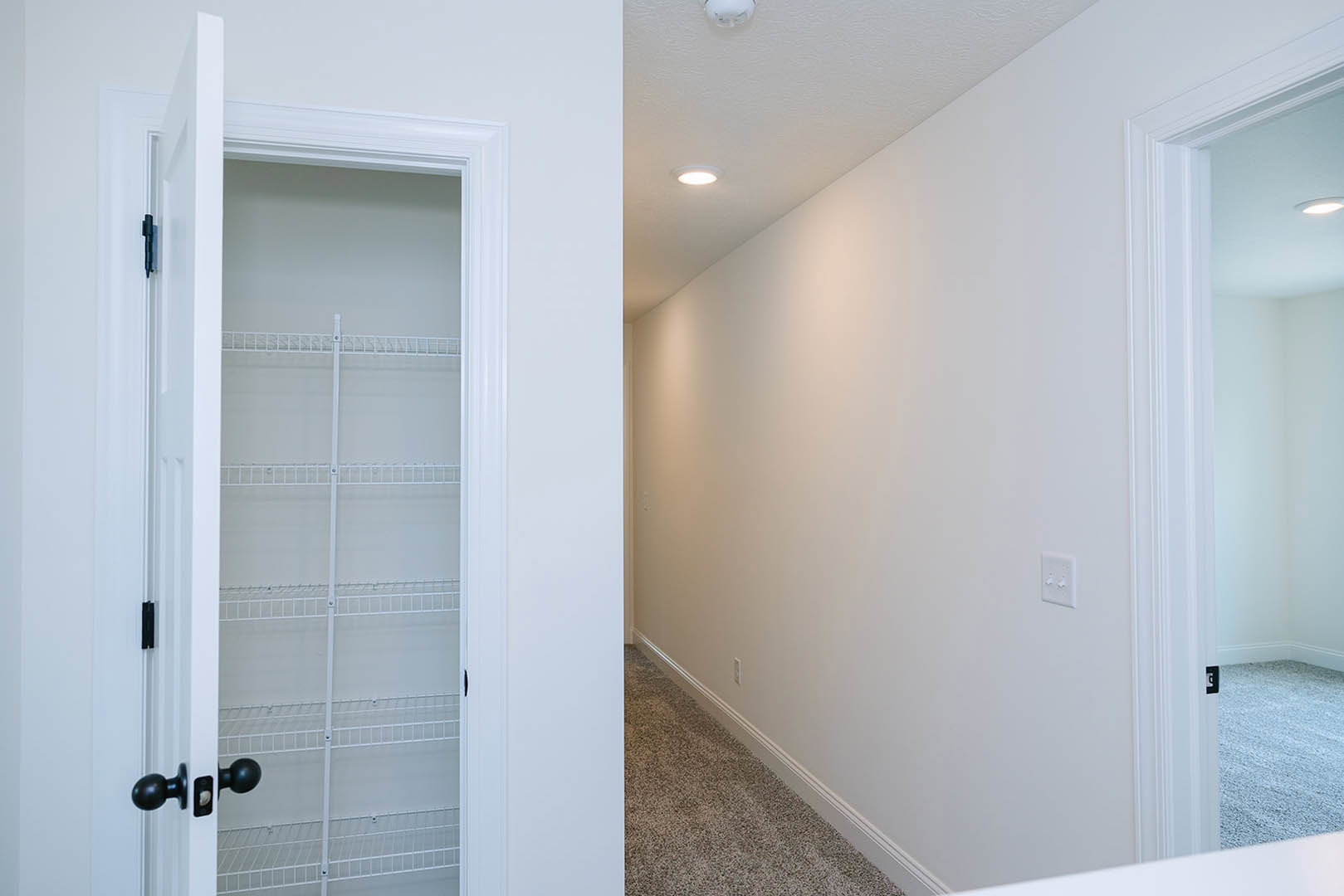 Hallway with light-colored walls, open white door featuring a black round knob, closet with white shelving, and white light switch with two knobs