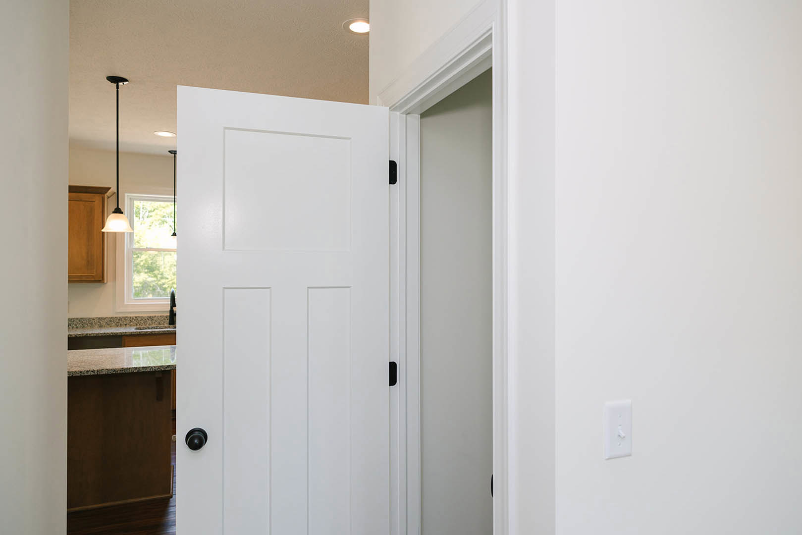 White paneled door with black knob opens to a room featuring white cabinetry, window with white frame, and white ceiling.