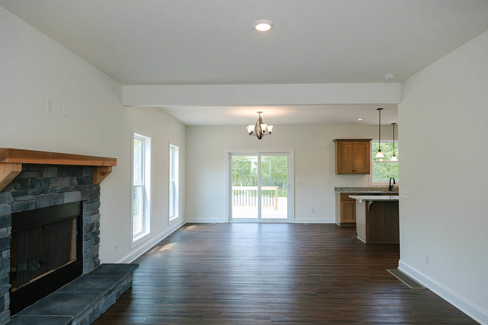 Living room with stone fireplace, hardwood floors, white walls, ceiling light, sliding glass door leading to outdoor deck, and modern lamp.