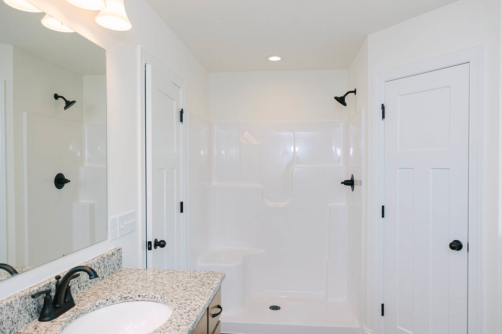 Modern bathroom with white tile walls, glass-enclosed shower, rectangular sink with chrome faucet, large wall mirror, and black light fixture above vanity