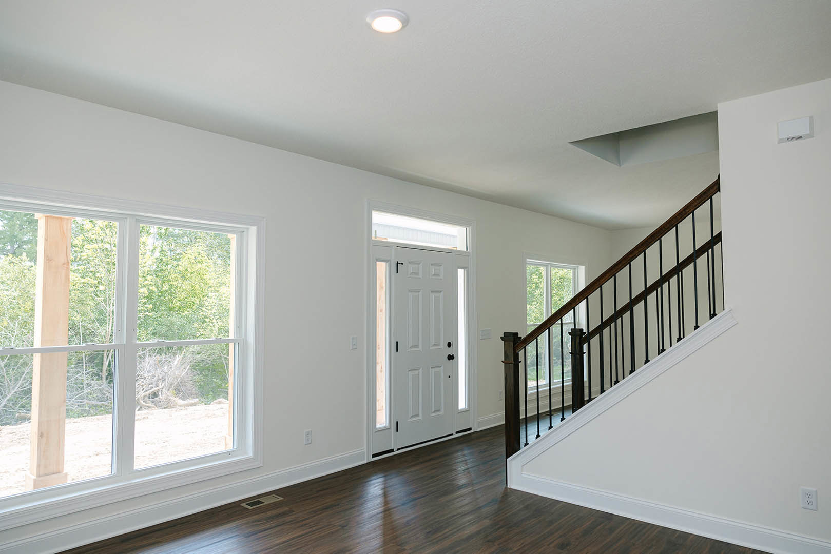White walls with plaster molding, black-railed staircase, white door with black knobs, wood beam above window, laminate flooring, ceiling light fixture