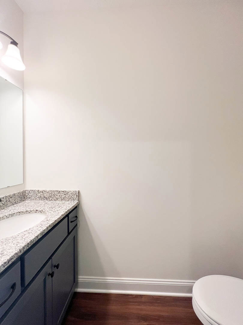 Modern bathroom featuring a white ceramic sink with chrome faucet, sleek toilet, light gray tile walls, wood vanity with drawers, and minimalist lighting fixture