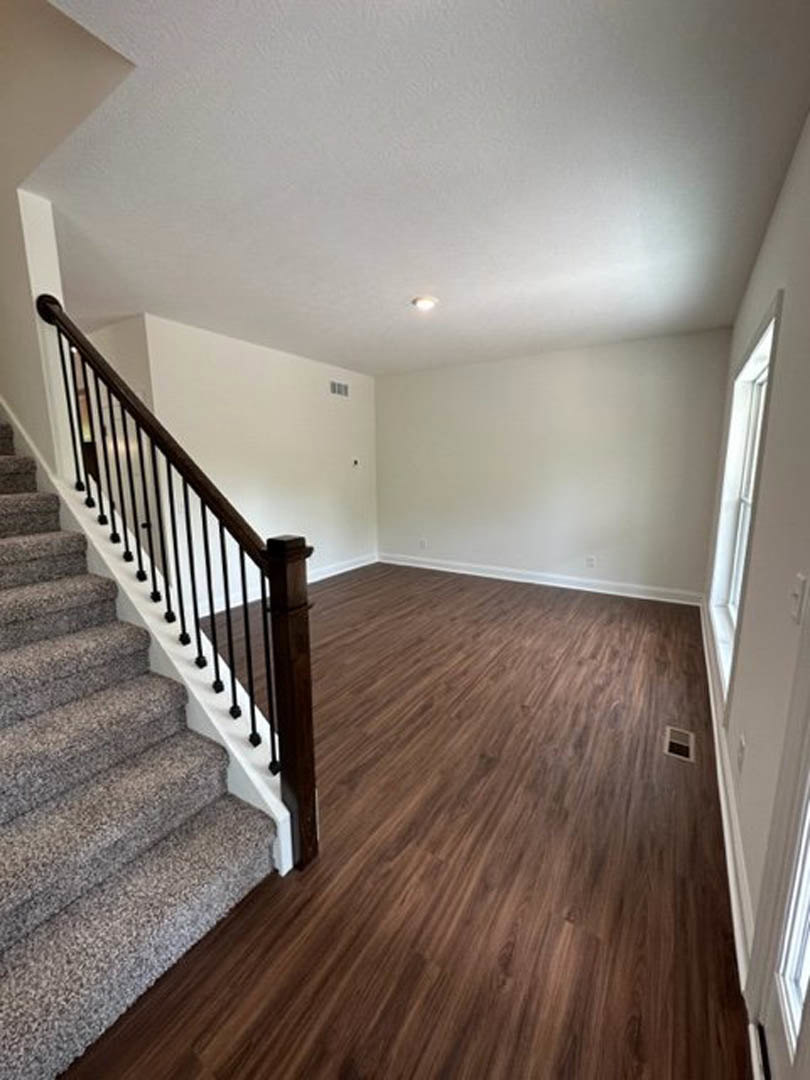 Hardwood staircase with white balusters, carpeted steps, adjacent window, and white ceiling with recessed lighting