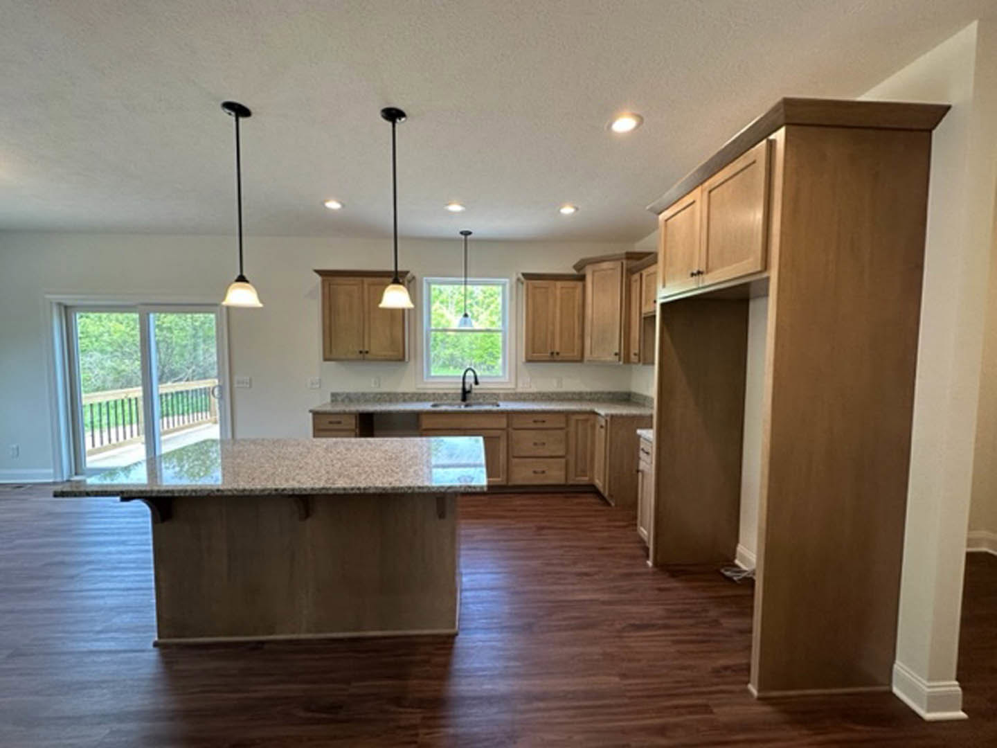 Spacious kitchen featuring a large central island with stone countertop, white cabinetry, stainless steel sink, hardwood flooring, and glass door windows allowing natural light