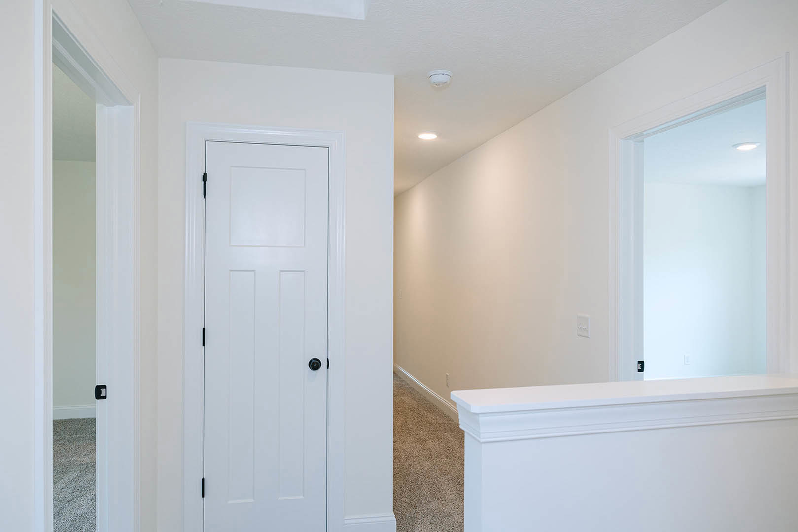 Hallway with white walls, white door featuring a black knob, white counter, ceiling light, and white railing