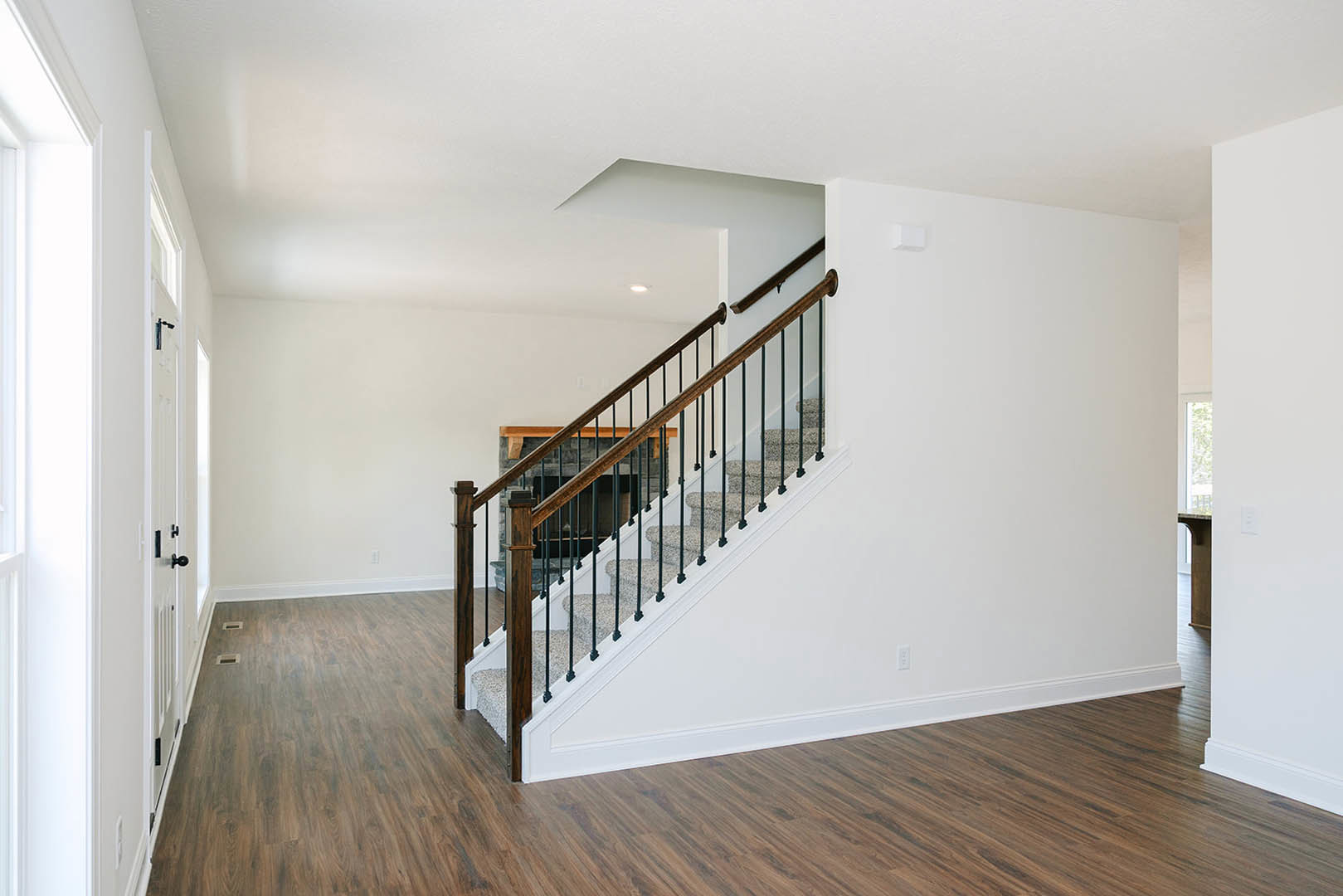 Carpeted staircase with black metal railings, wood flooring, white plaster walls, and a window allowing natural light.