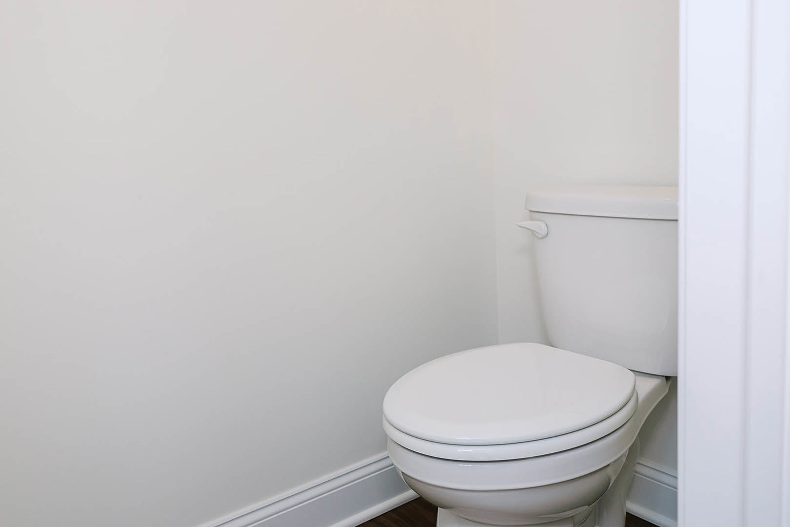 White toilet with closed lid positioned in a bathroom corner, white tile walls and floor visible.