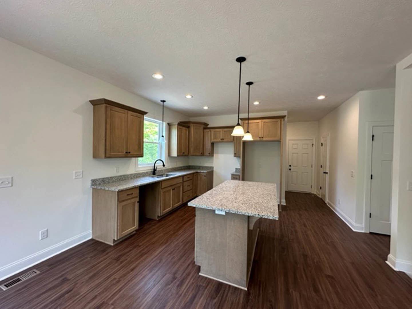 Marble kitchen island with waterfall edge, wood plank flooring, white cabinetry, black hardware, stainless steel sink, and large window letting in natural light