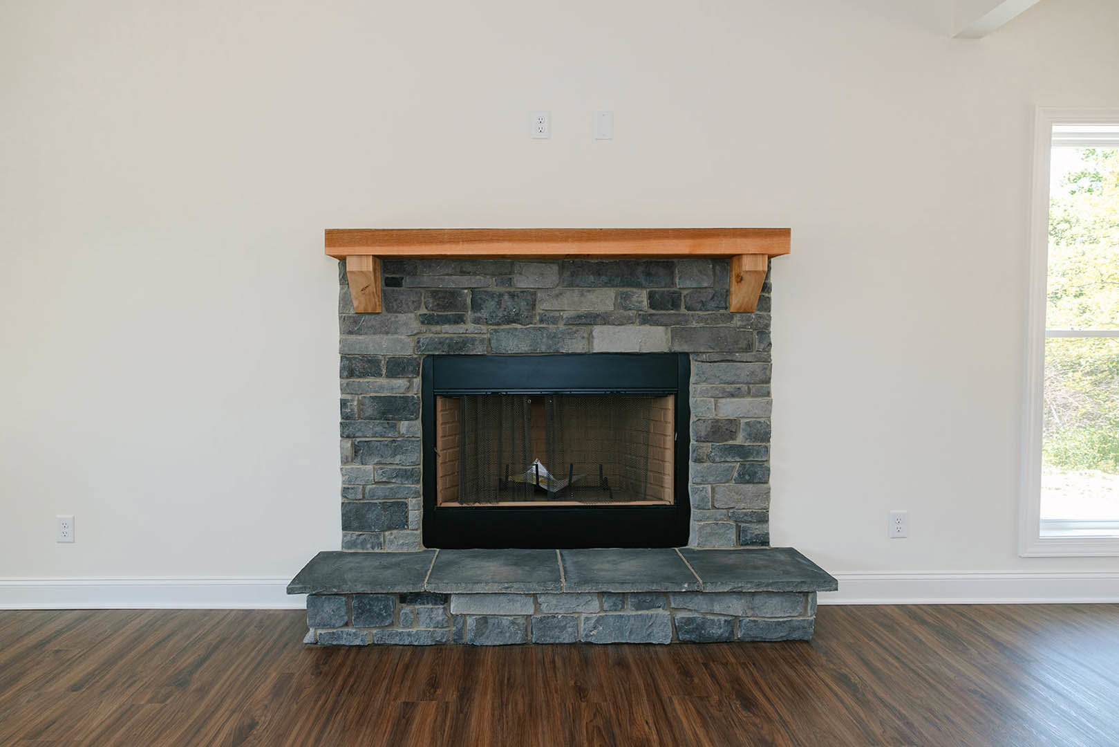 Stone fireplace with wood mantel, wood floor, and brick accent wall in a cozy living room.
